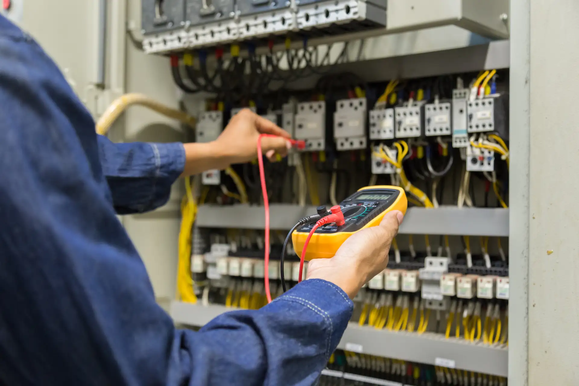 Un ingeniero electricista realiza pruebas de medición de voltaje, corriente y potencia en una línea eléctrica, mientras controla un gabinete eléctrico